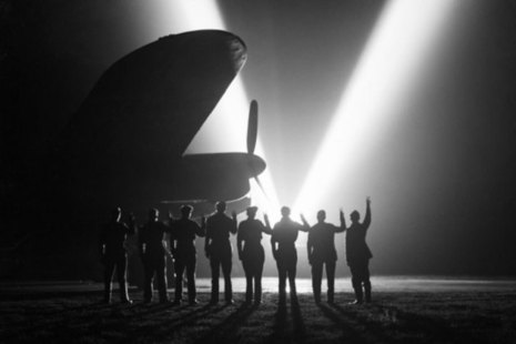 Ground crew on a RAF Bomber Command station in Britain return the V-sign to a neighbouring searchlight crew . Silhouetted is the nose of a Lancaster. [Picture: Imperial War Museum CH 15165]