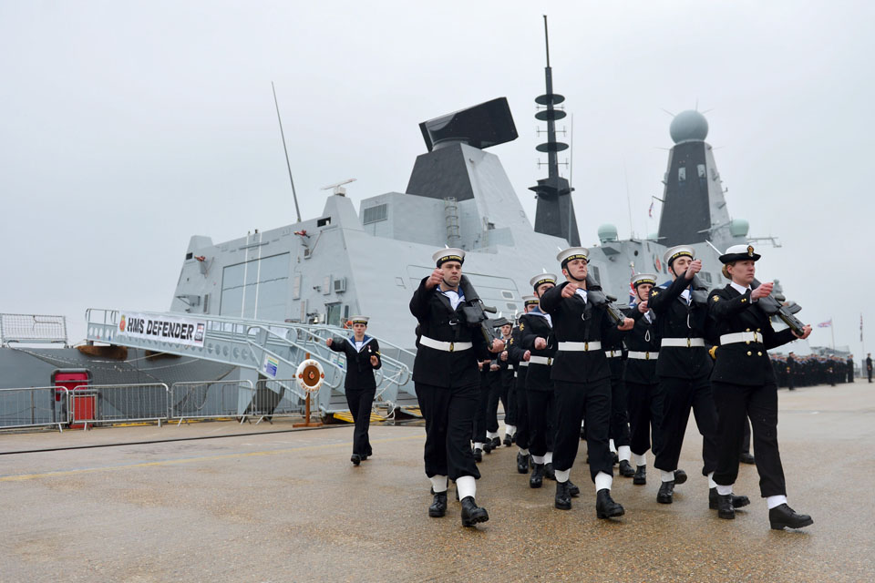 A ceremonial guard marches past HMS Defender
