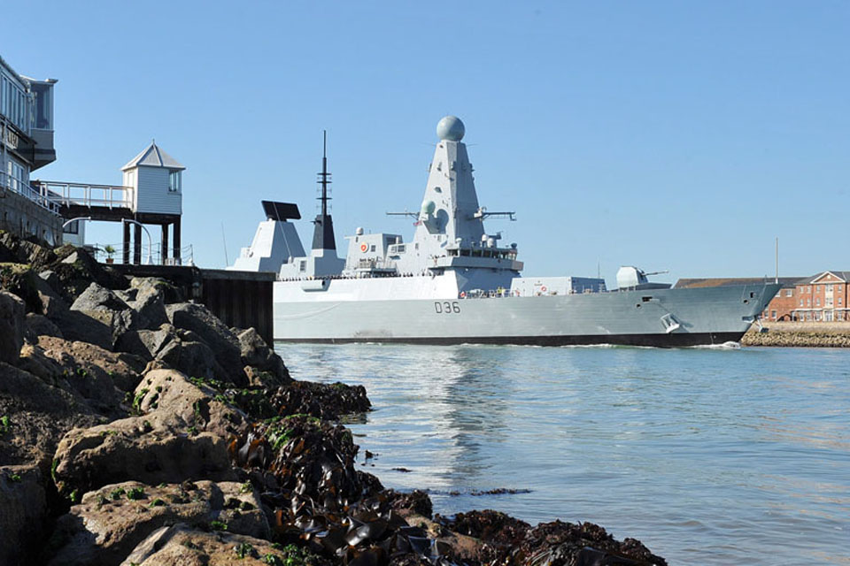 HMS Defender passes between the harbour walls at Portsmouth