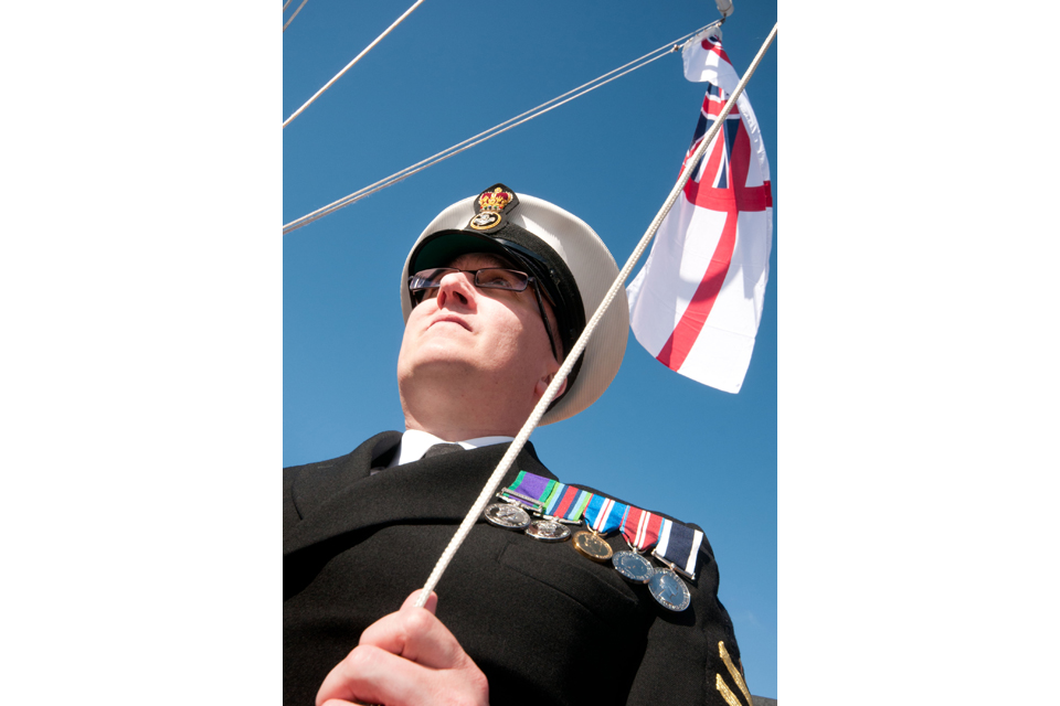 A Royal Navy reservist hoists the White Ensign at HMS Dalriada