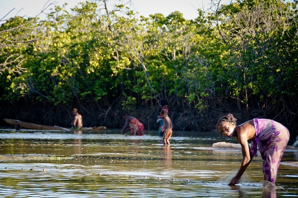 Men, women and children in water laying out fishing nets