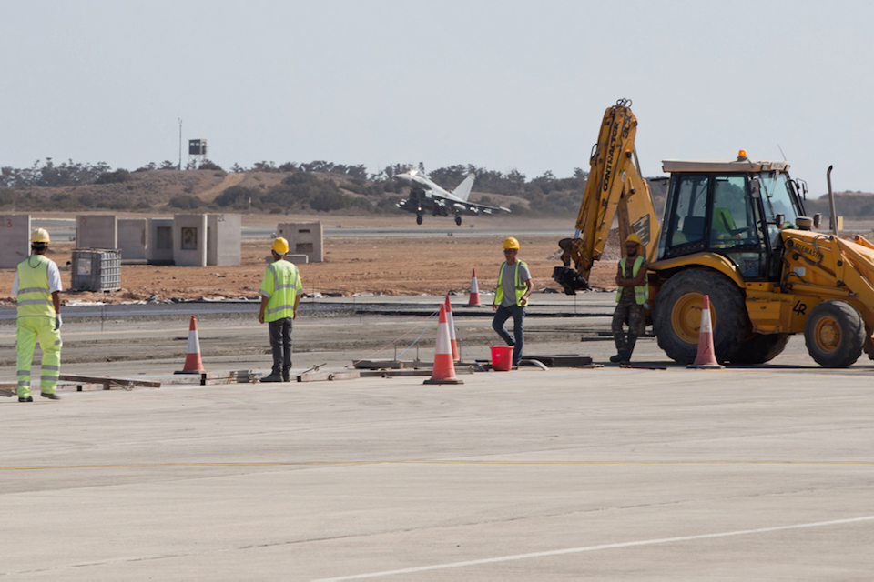 A Typhoon takes off as building contractors look on.