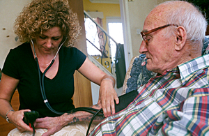 Carer taking an older man's pulse in his home