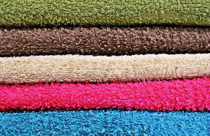 A pile of 5 different coloured towels. Colours from top to bottom are: green, brown, beige, pink and blue.
