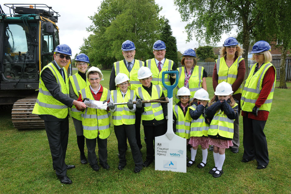 Pupils and contruction workers holding a spade to mark the cutting of turf at the school