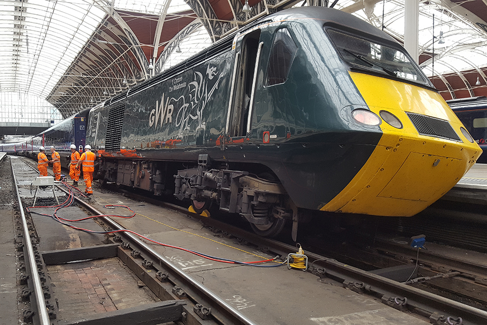 Derailed power car at Paddington station in blue GWR livery. Four engineers in high visibility clothing are working alongside the train