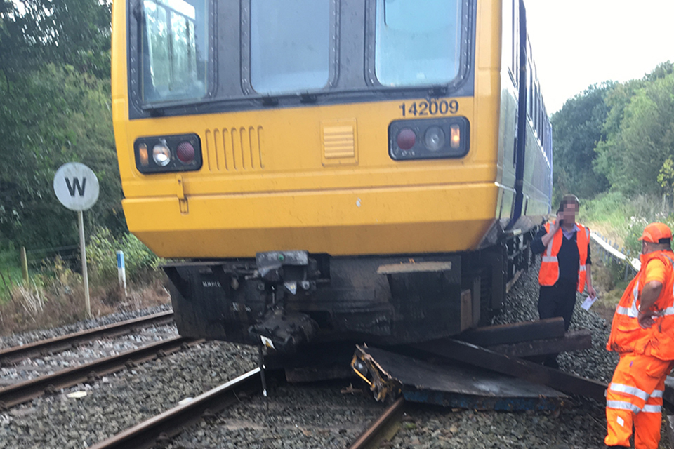 View of the front of train after collision with the trolleys. The trolley is under the train. Railway staff in high visibility clothing are standing next to the train. a