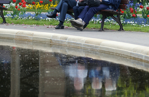 Three people sitting on a bench - their reflections displayed in a pond