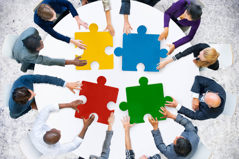 group of people around a round table linking large jigsaw puzzle pieces together
