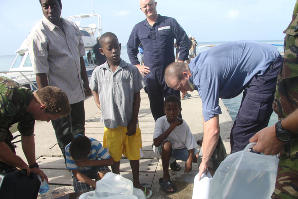 Crew members from HMS Manchester distribute fresh drinking water to locals