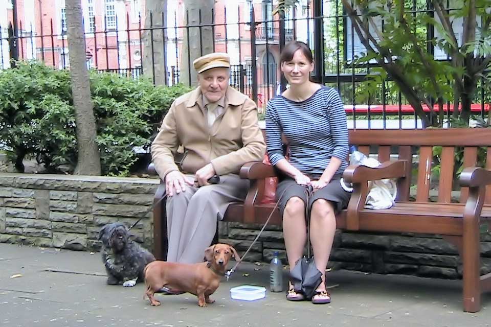 2 people seated on a garden bench with dogs at their feet