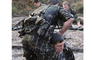 One of the Royal Marines Physical Training Instructors is helped out of a submerged water pipe during the Tarzan assault course phase of the four commando tests