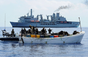 Royal Marines search a pirate skiff packed with fuel drums with RFA Fort Victoria in the background