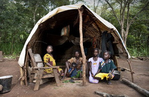 A family sit in a makeshift shelter in a forest clearing