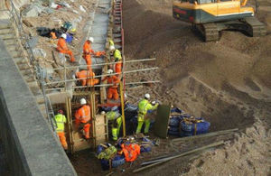 A dozen builders in fluorescent overalls and white helmets on scaffolding, fixing the wall on the beach