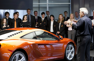 Man talking to young people and teachers around a McLaren car