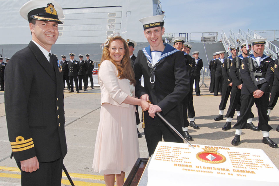 From left: Commanding Officer of HMS Diamond, Commander Ian Clarke, watches as his wife Joanne and the youngest member of the ship's company, Engineering Technician Ross Hindmarch, cut the commissioning cake