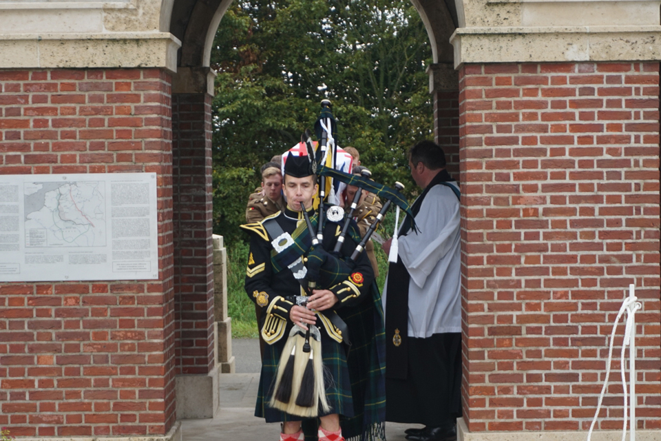 Local piper, Pierre Dervaux, leads the procession into the cemetery - Crown Copyright, All Rights Reserved