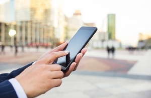 arm of business woman holding mobile phone against busy street background