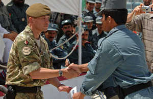 Soldier presents a graduation certificate to an Afghan policeman