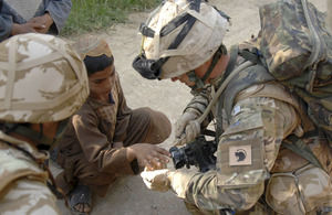 Lance Corporal McLoughlin cleans a cut on a local boy's hand with the water from his CamelBak drinking system