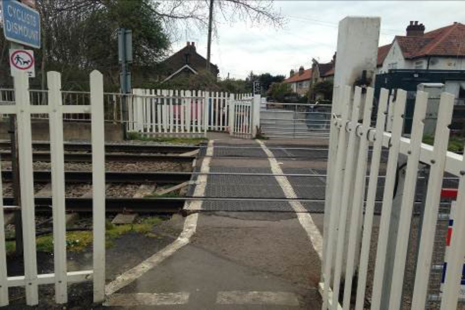 Trinity Lane footpath crossing (courtesy of Network Rail) showing the path across two railway line. White picket fencing in the foreground and middle distance with house beyond.