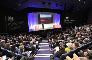 A speaker on stage in front of an audience of people.