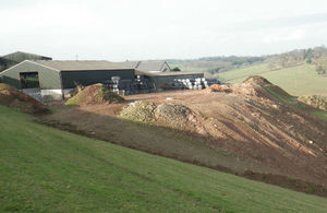 Huge mounds of rubble in front of hilltop farm surrounded by green pastures