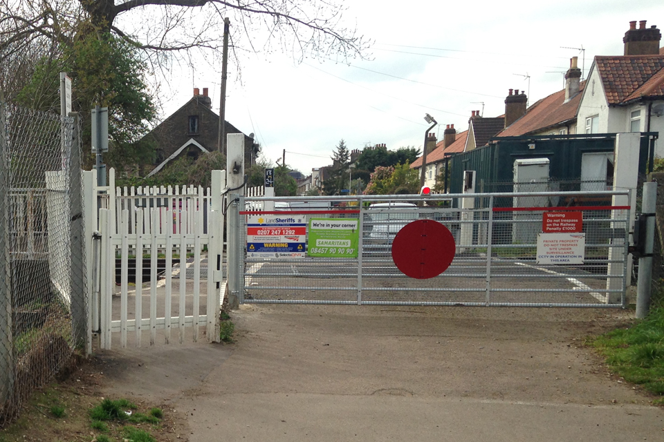 Trinity Lane footpath and vehicle level crossings, from the east (image courtesy of Network Rail) showing the gate for pedestrians and a large metal gate, with a ref light and large red circle for vehicle users