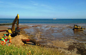 Sand being pumped out of a pipe onto Dawlish Warren beach with construction workers in background