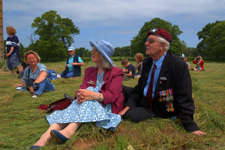 Picnicking veterans watch paratroopers jump over Normandy