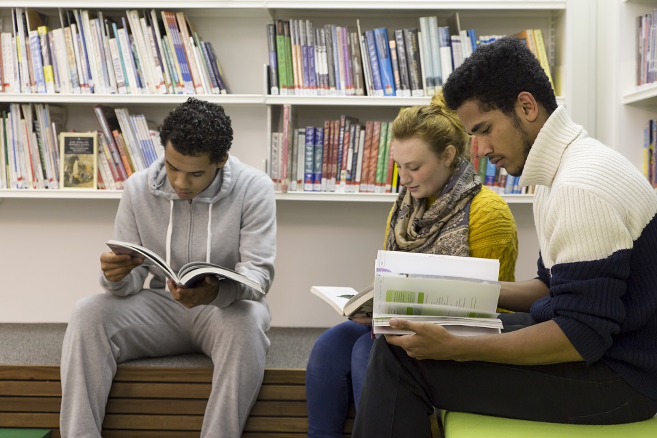 Three students looking at books in a library