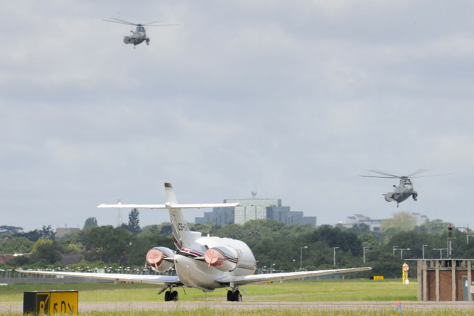 Two Royal Navy Sea King helicopters landing at RAF Northolt with a civilian aircraft in the foreground 