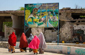 Somali woman walk past a billboard mural. AU-UN IST PHOTO / STUART PRICE