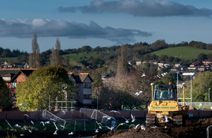 A digger on a flood embankment as part of the new Exeter flood defence, with new flood wall in the background