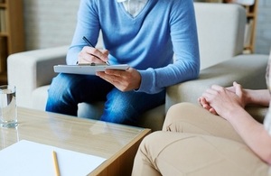 Two people sitting on armchairs having a discussion. One is writing on a clipboard.