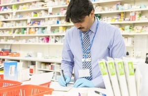 A male pharmacist behind the counter checks a prescription.