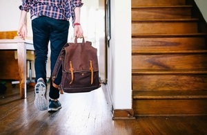Teenager holding bag, seen from the back, in a house.