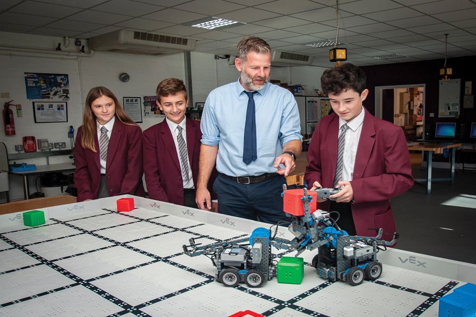 Pupil with remote-controlled model vehicles, standing with two other pupils and teacher