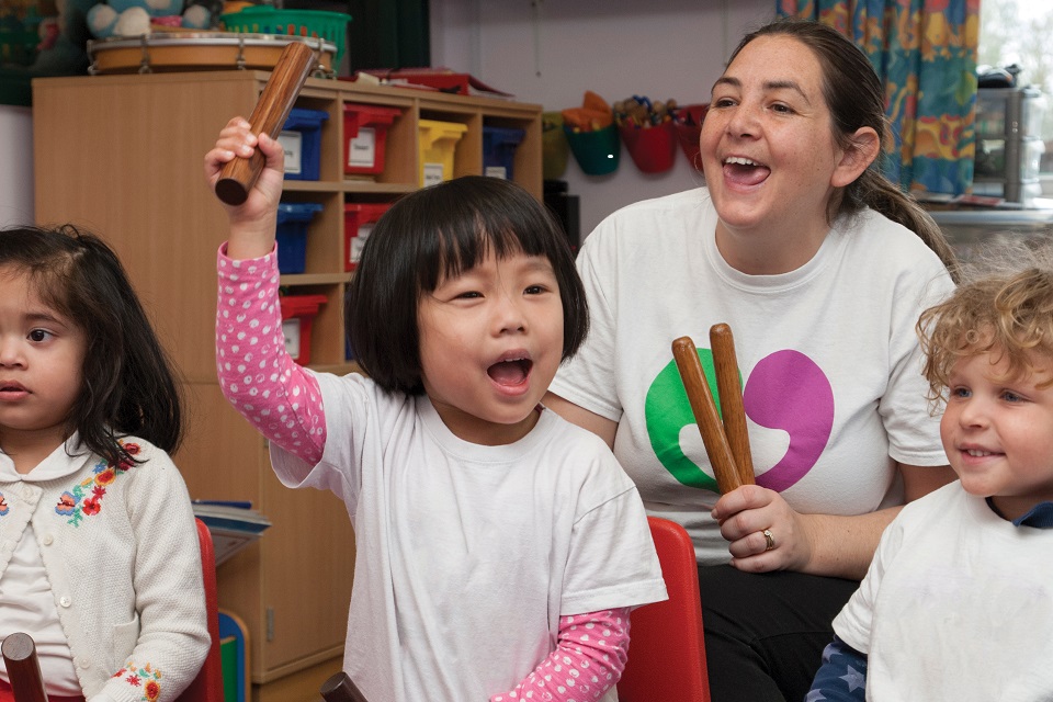 Three young children taking part in musical activity with childcare professional