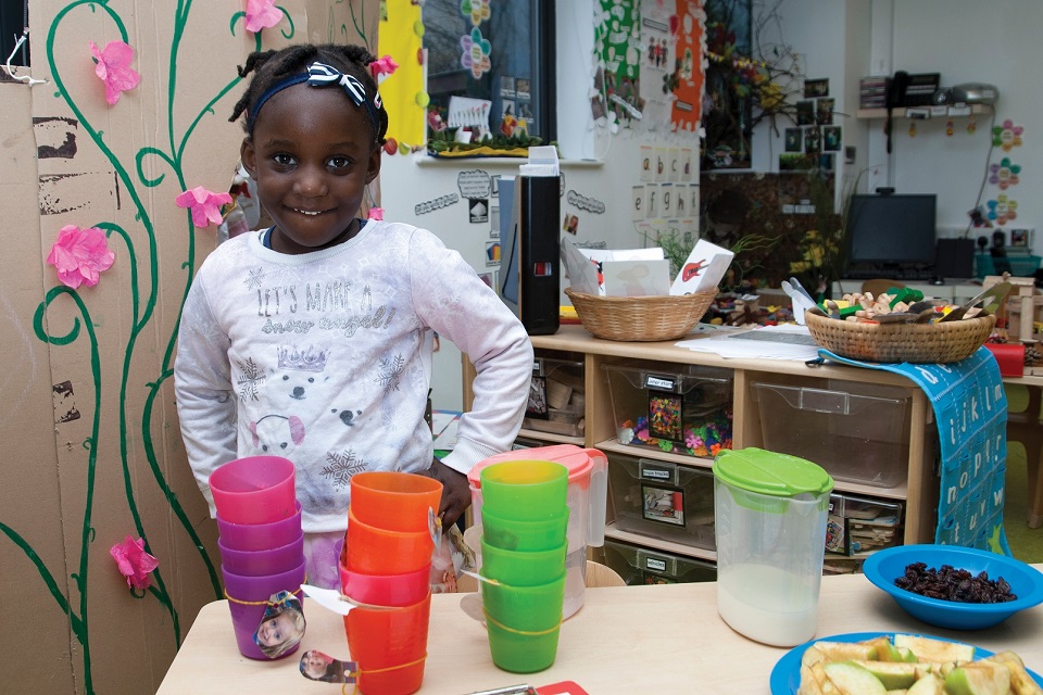 Young girl in nursery standing in front of table with lots of coloured cups