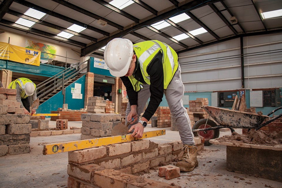 Student in hard hat and high-visibility jacket checking the level of bricklaying