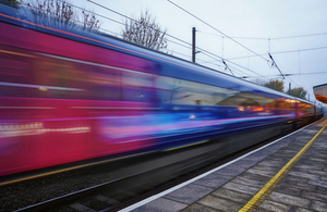 An image of a train traveling past a railway station platform.
