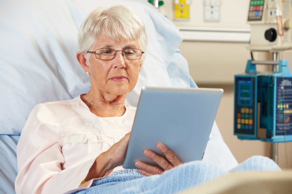 Older lady in bed using iPad in hospital