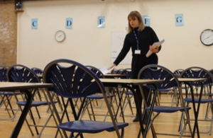 A woman handing out papers in an empty exam hall
