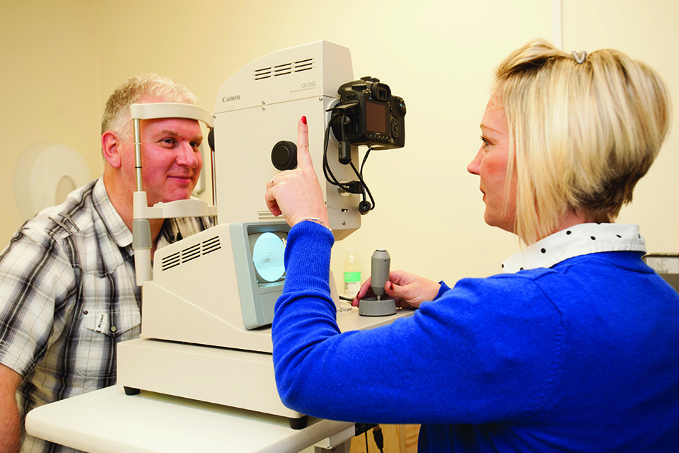 Photo of a male patient being screened by a female diabetic eye screener who is using a digital screening camera