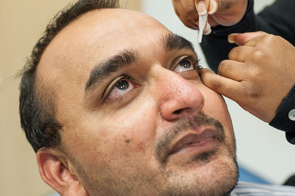 Photo of eye drops being administered into an eye before screening