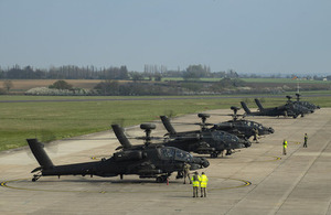 Apache attacked helicopters line up side-by-side on an airfield