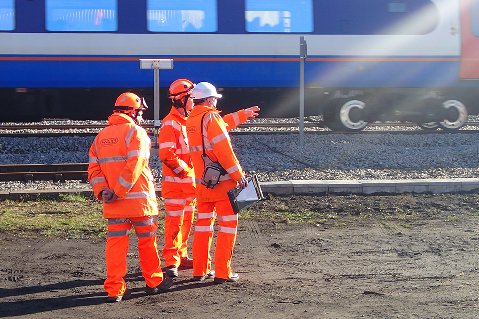 Three RAIB staff in high visibility standing in a position of safety as a train passes by.