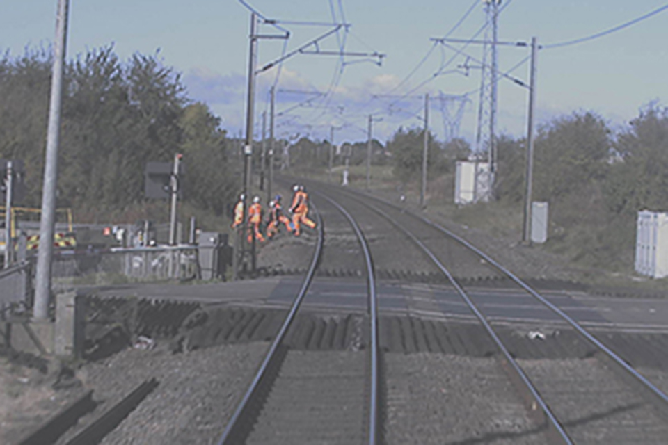 View from forward facing CCTV showing trackerworkers moving into the left-hand cess at Egmanton. A crossing is in the foreground and OLE is visible